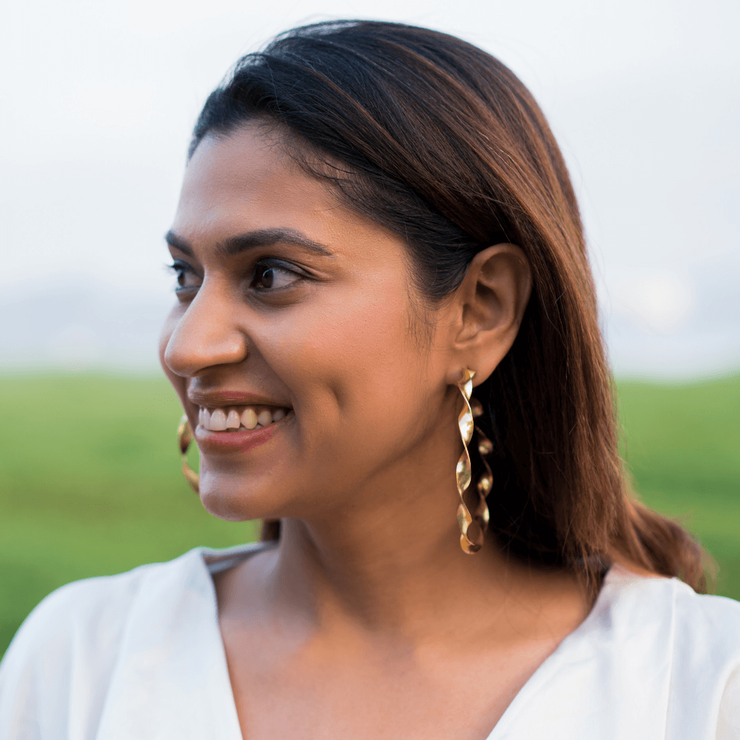 Model wearing big twirl gold hoop brass earrings in open fields. 